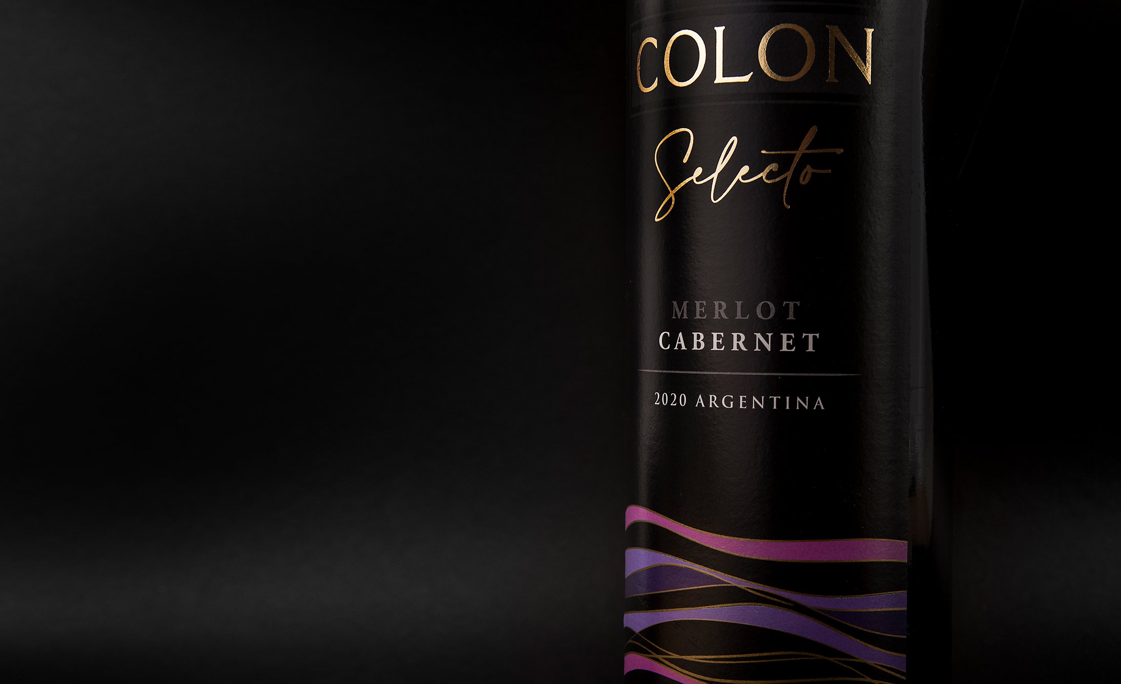 Sleek black wine bottle with "Colon Selecto" label in elegant gold and white text. Vibrant purple and pink wave design at the base suggests sophistication.