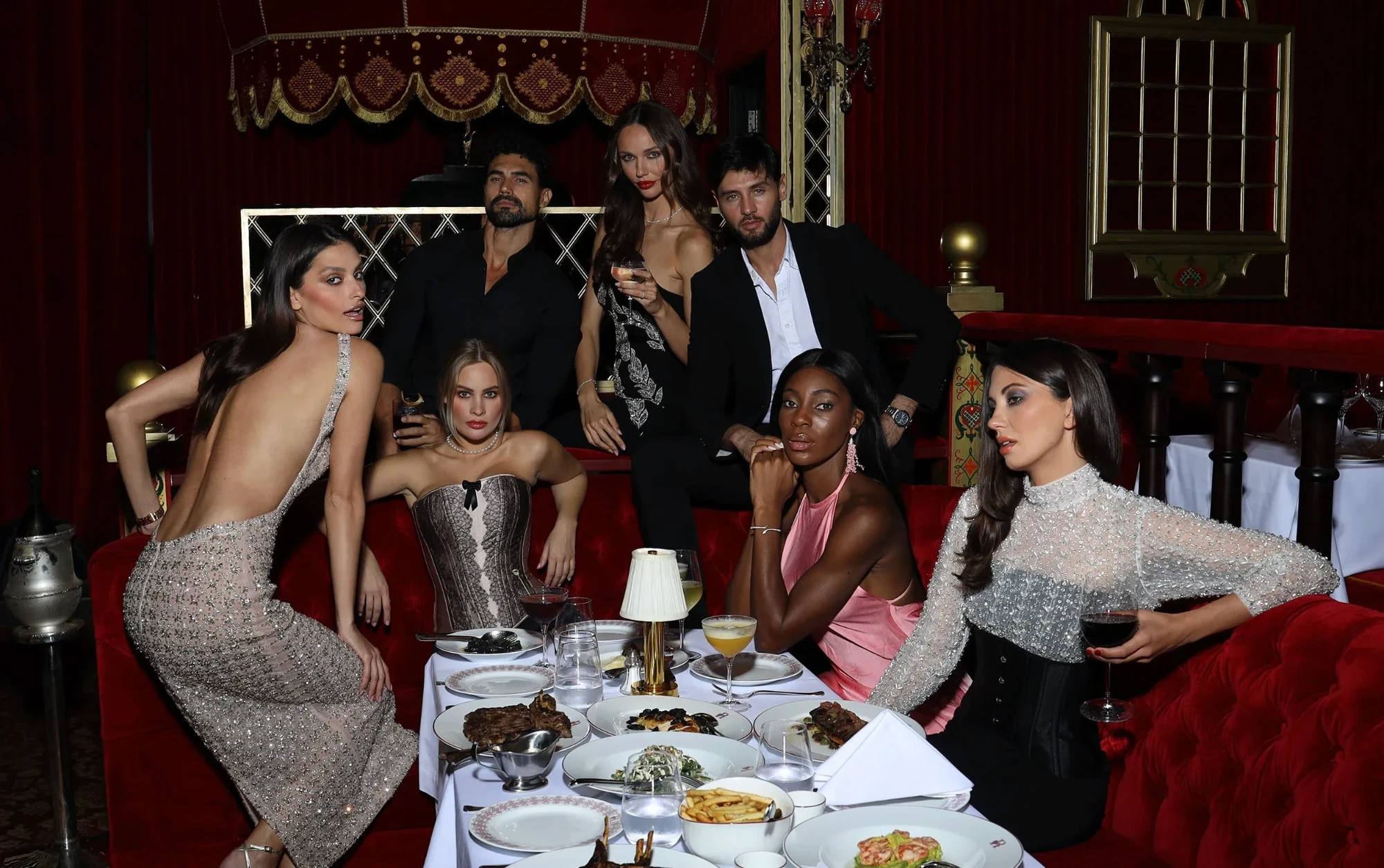 Guests dressed up around a dinner table on red velvet banquettes at Raspoutine Dubai