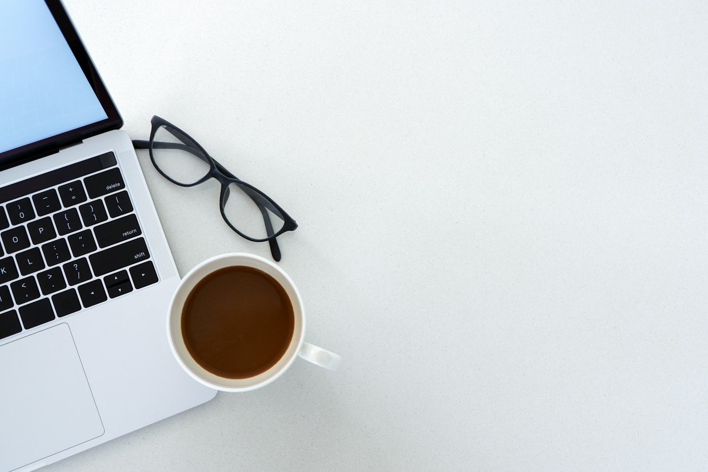 Laptop, glasses and coffee on a white desk seen from above
