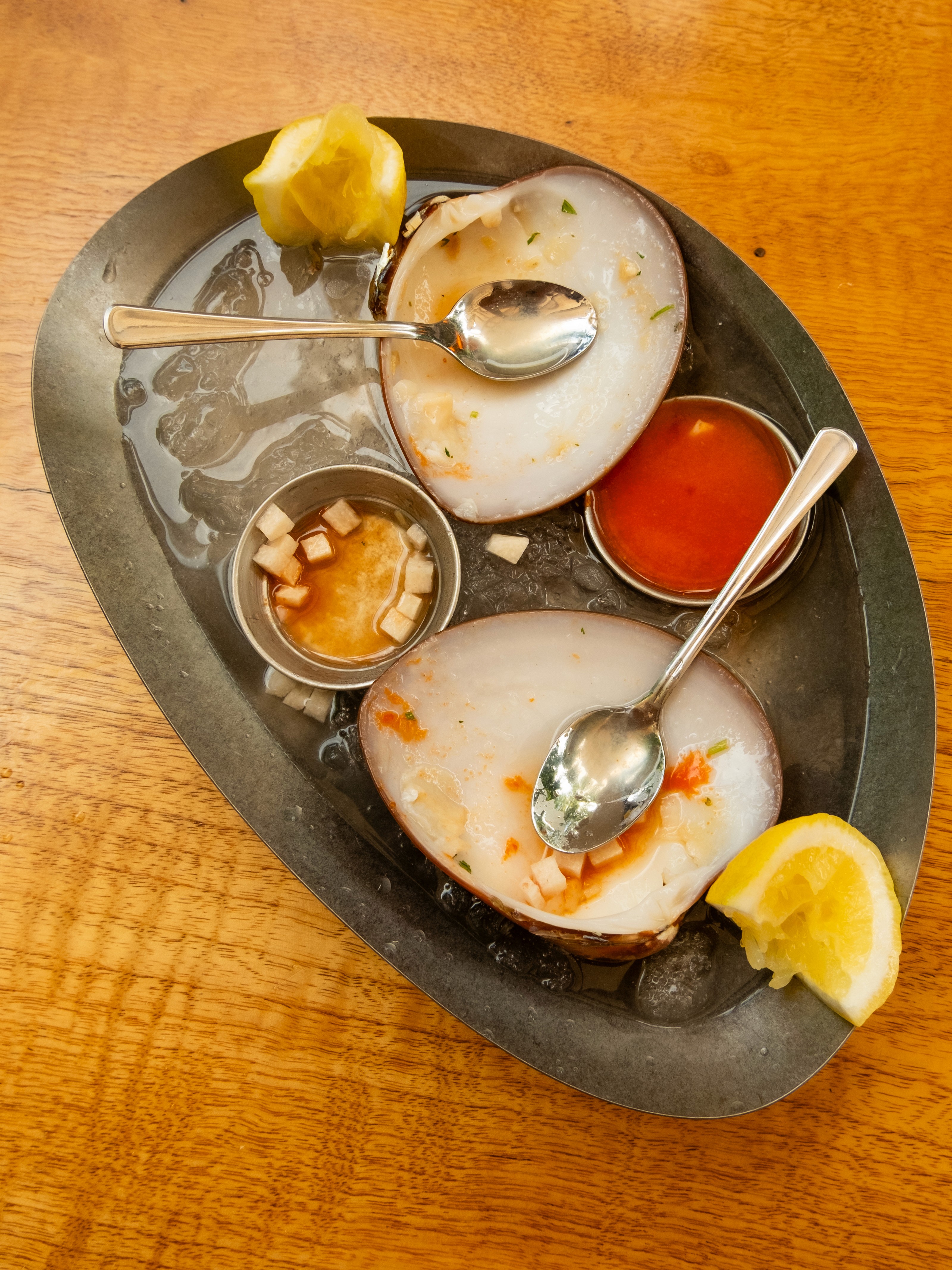 White plate with roasted chicken served in a golden sauce with herbs and capers, placed on a terrazzo tabletop in sunlight.