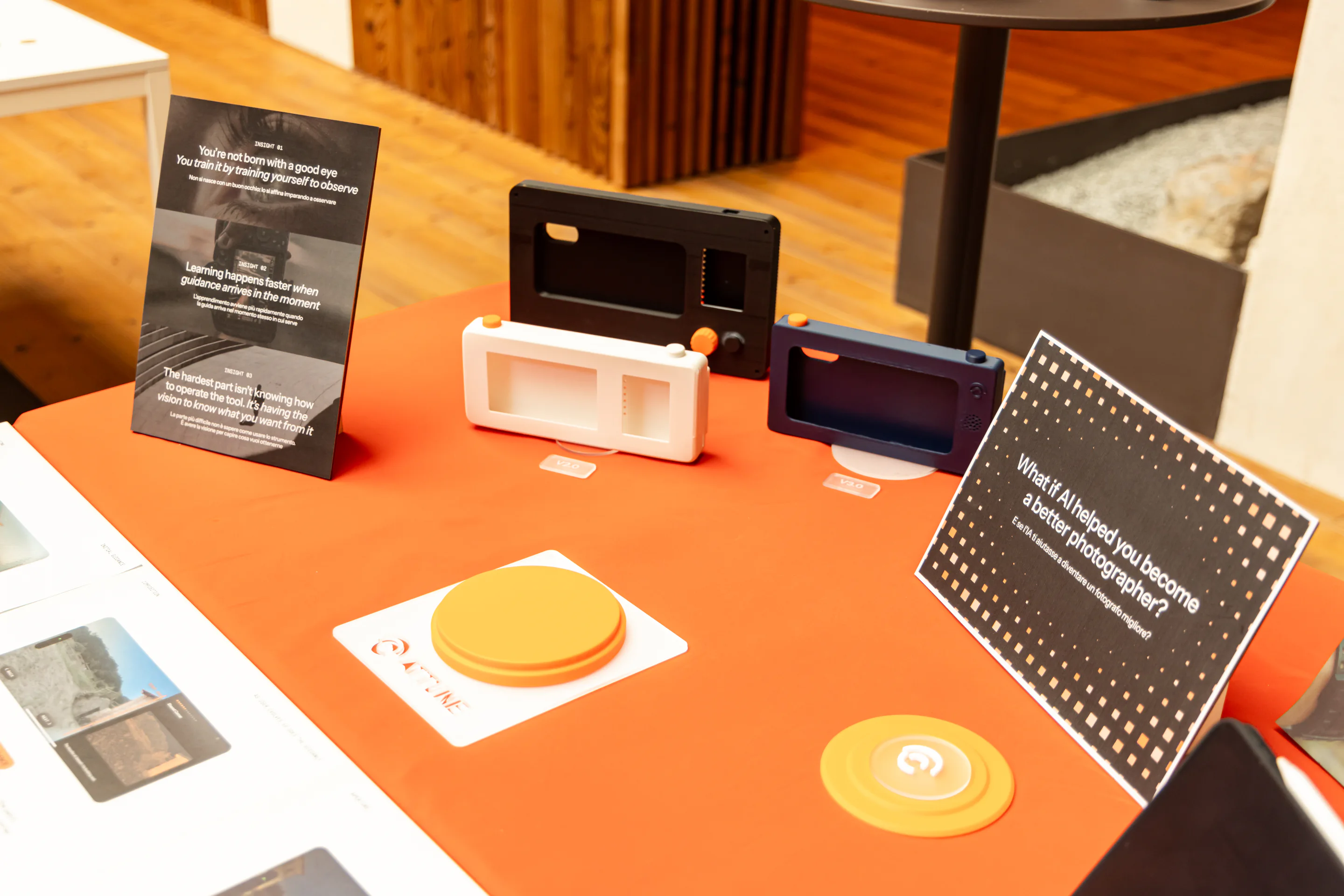 An orange exhibition table displays three Attune camera prototypes, project insight boards, and circular interaction objects.