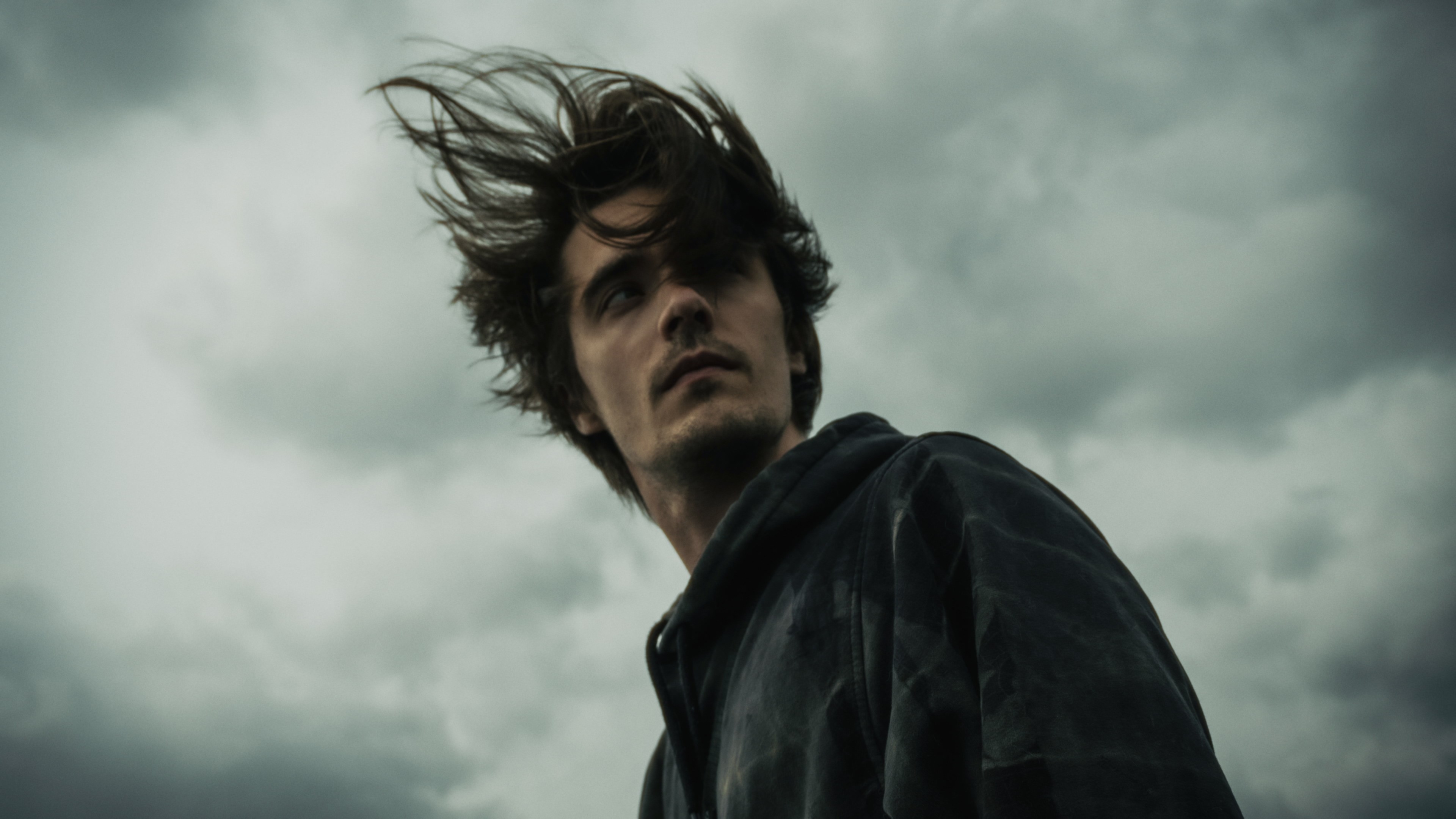 Low angle portrait of a man with windblown hair looking away, moody atmosphere.