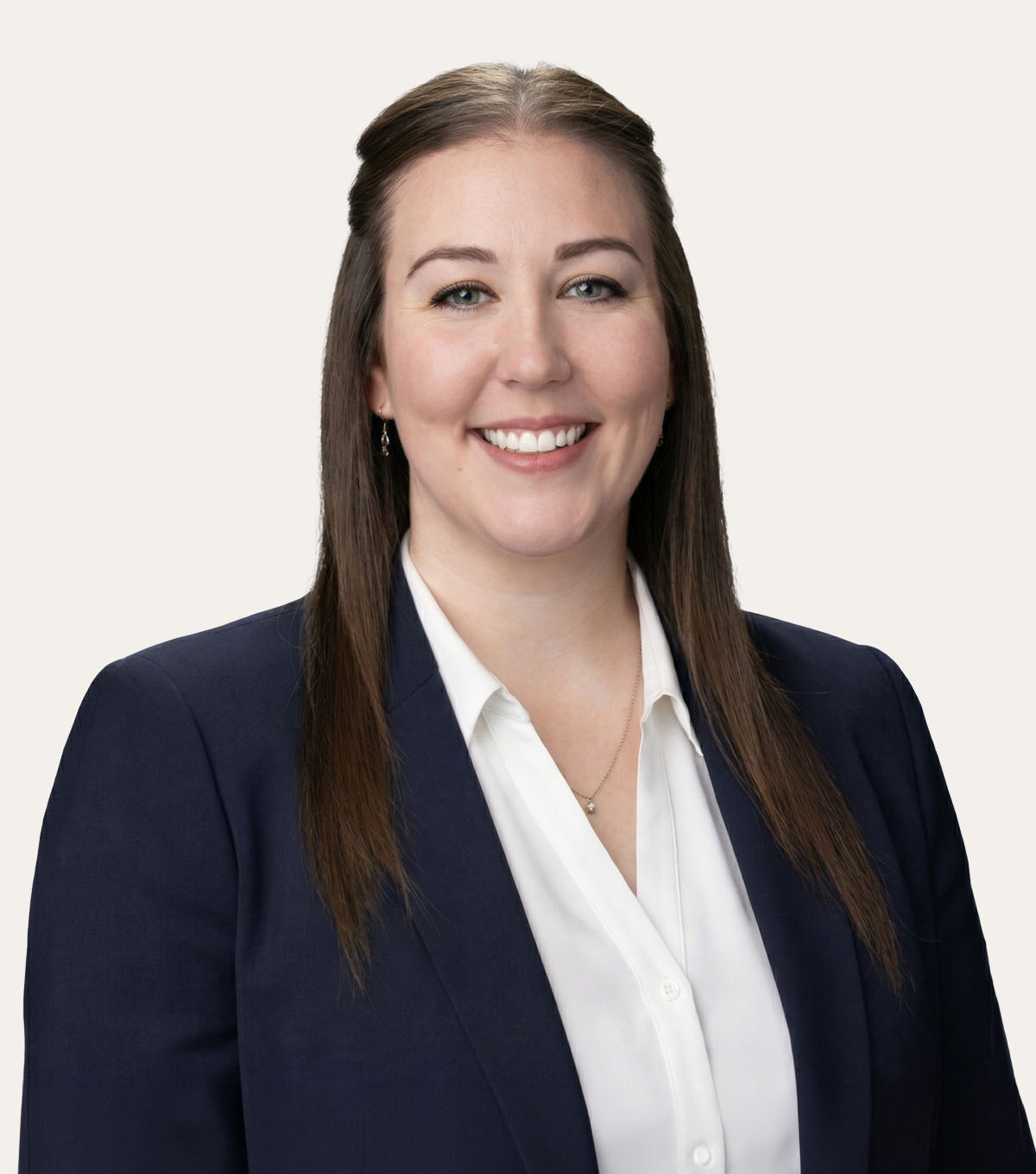 A woman with long brown hair wearing a white button-up shirt and a navy blazer smiles at the camera.