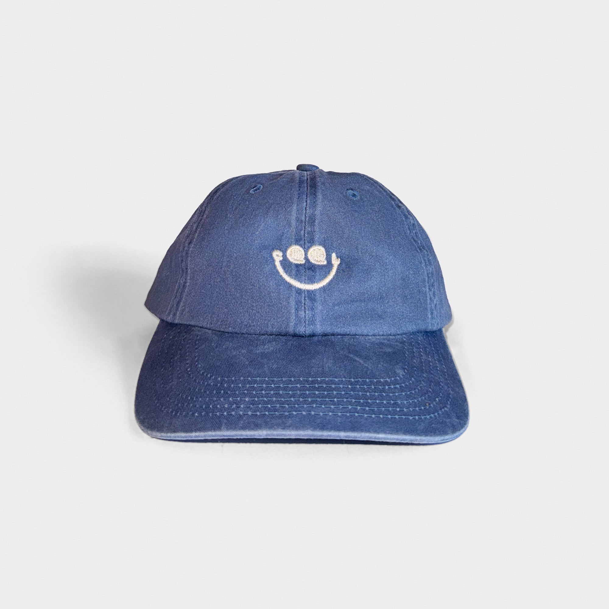 Blue denim cap with a smiley face design on a light gray background