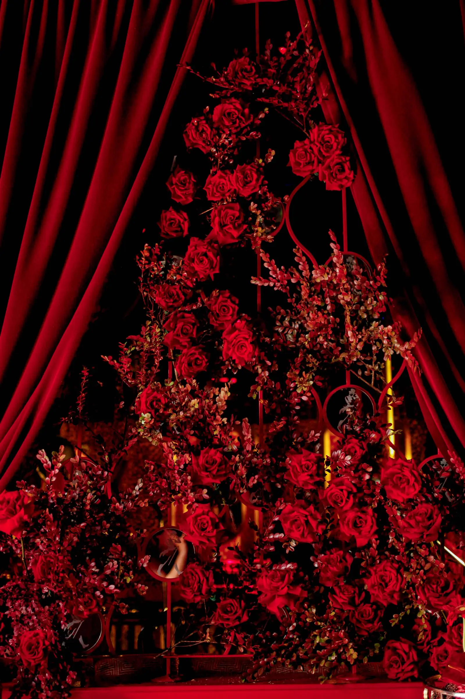 Arco floral de rosas rojas silvestres enmarcado por cortinas de terciopelo para altar o escenario de boda.