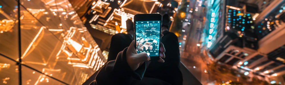 Person capturing cityscape from high vantage point with smartphone at night.