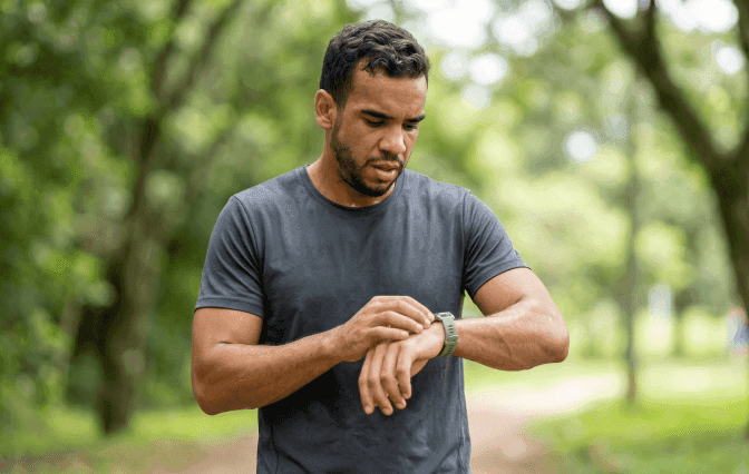 Corredor parado no parque olhando para o relógio e confuso sobre seu treino de corrida de rua.