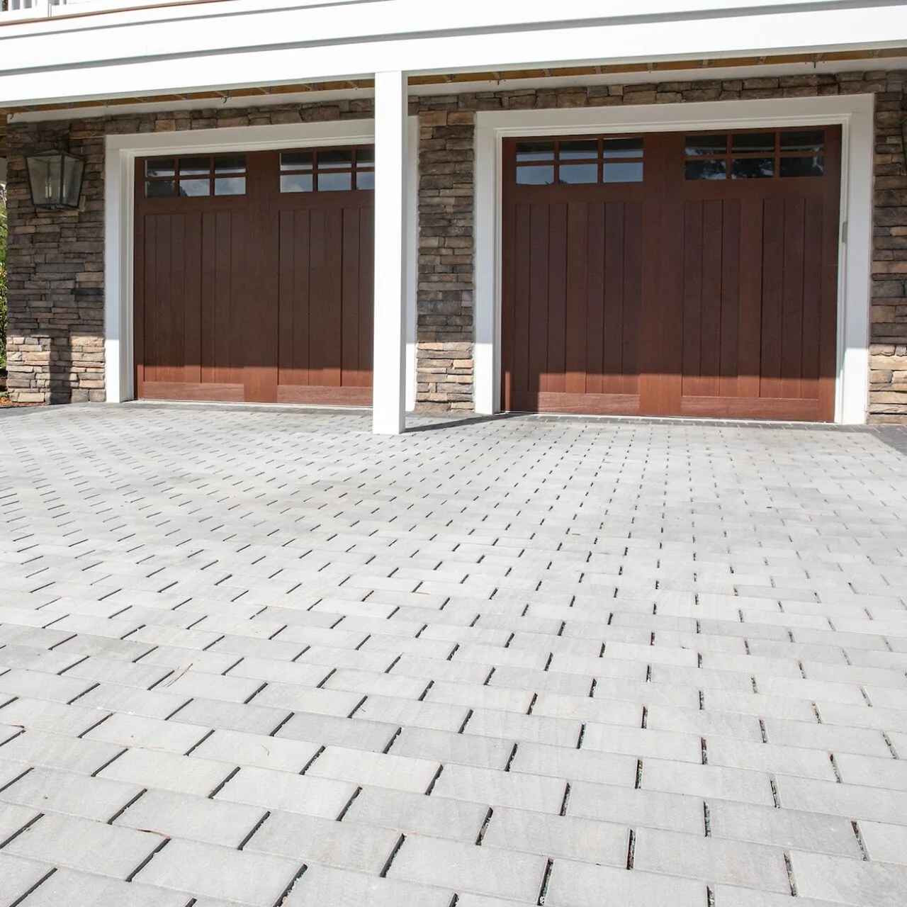 A bright driveway finish Light rectangular pavers laid in front of two wooden garage doors.