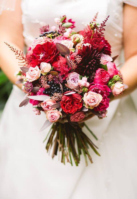 A vibrant bridal bouquet featuring a mix of red, pink, and purple flowers.