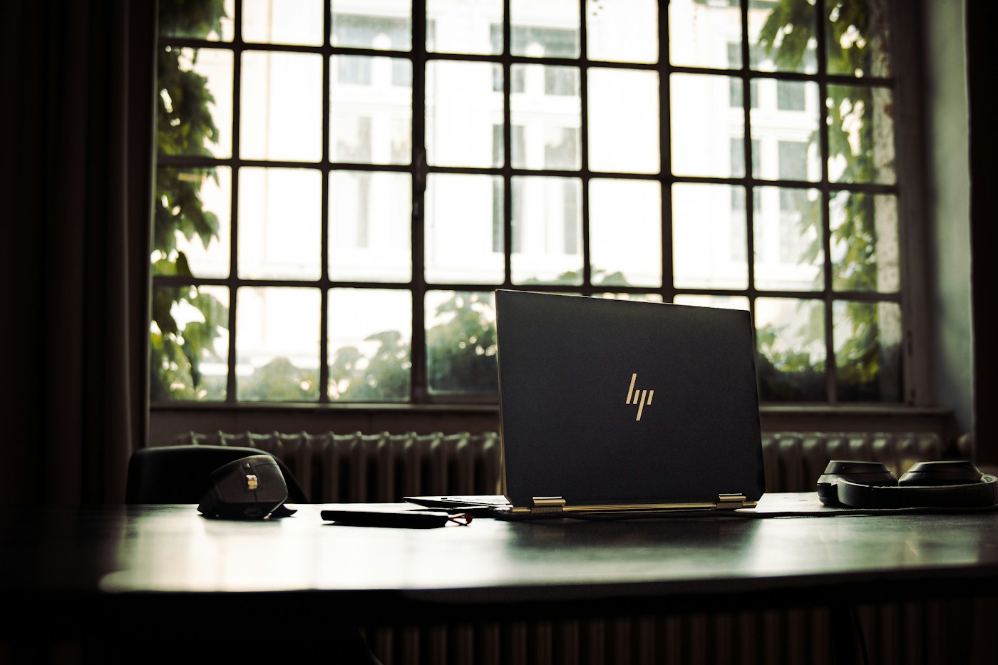 laptop on a wooden desk plugged into a charger by a window