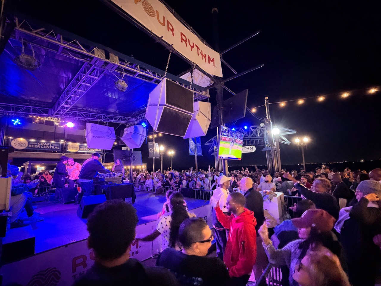 A wide nighttime view of the Navy Pier Beer Garden stage and crowd under blue and purple lighting.
