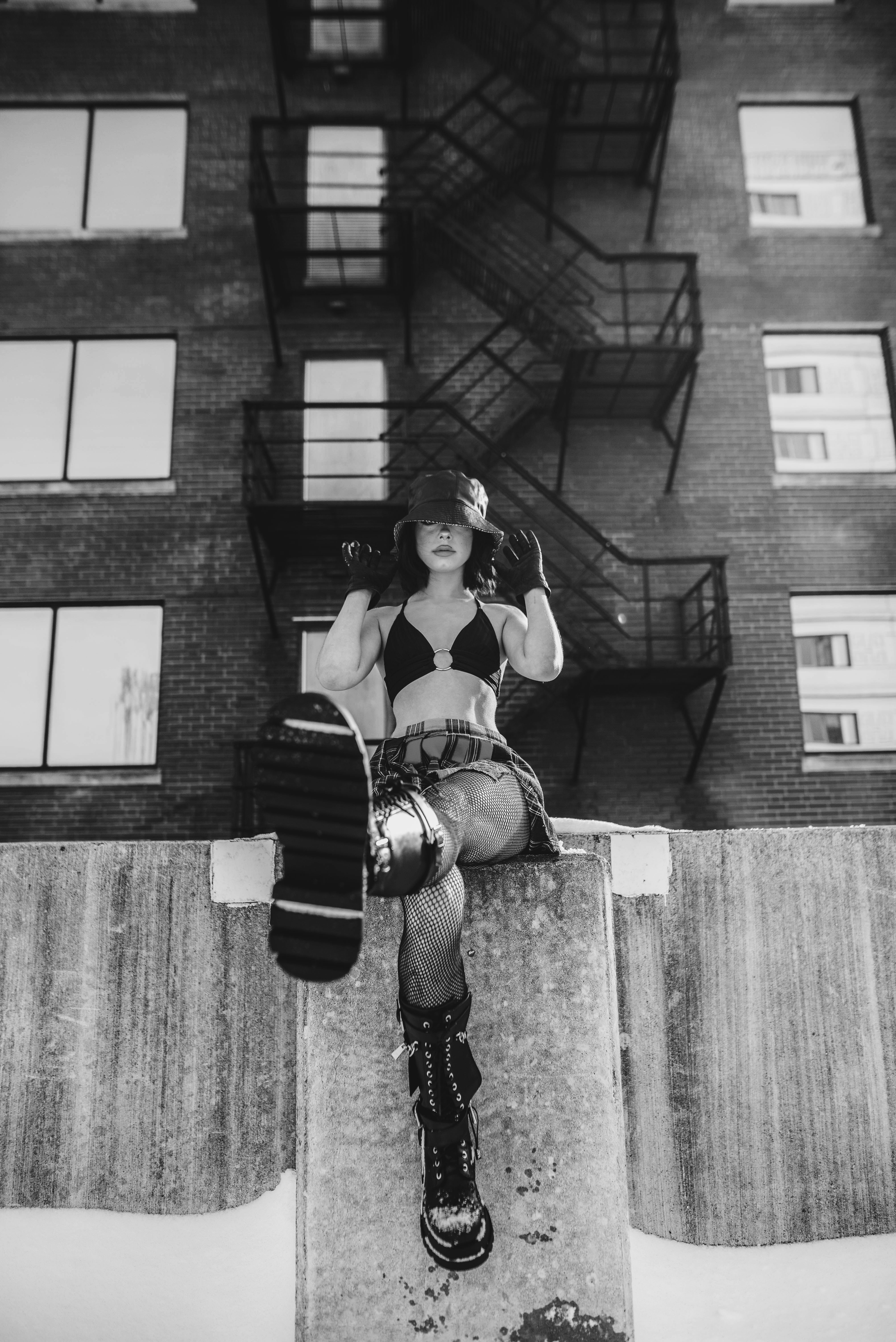Black and white portrait of Angel sitting on a concrete ledge in an urban setting, symbolizing strength, visibility, and a confident stage identity.