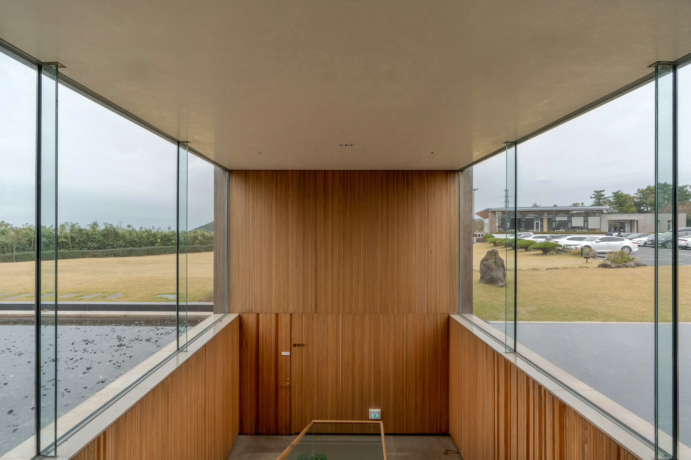 Modern interior entrance with floor-to-ceiling glass walls and warm timber cladding overlooking landscape