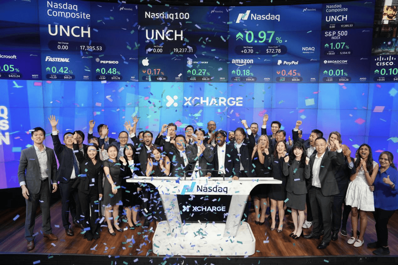 XCharge team celebrates on a stage with confetti standing between a Nasdaq podium and large screen displaying the XCharge logo.