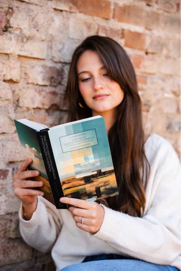 A woman with long hair and a black blazer holds a copy of Boethius's "The Consolation of Philosophy" next to her face, published by Logos.