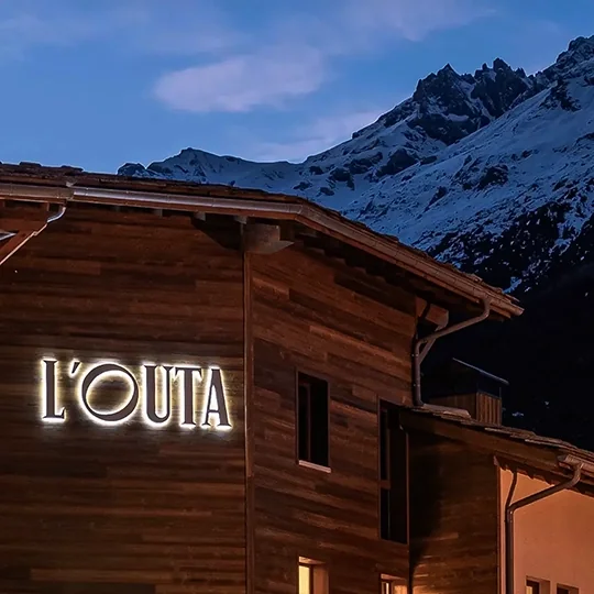 Enseigne lumineuse de l'hôtel de montagne l'Outa à la tombée de la nuit.