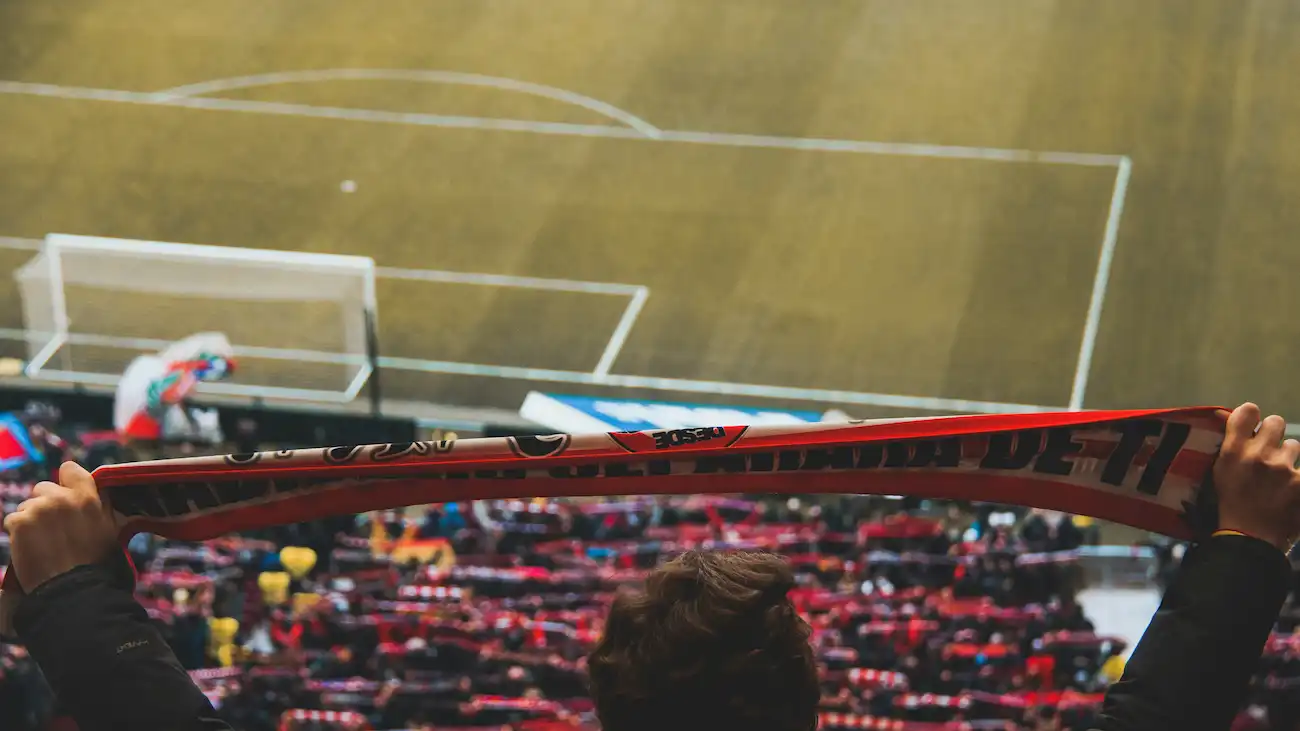 Football supporter holding a club scarf above the stands, representing fan merchandise, loyalty campaigns, supporter identity and fan retention for sports clubs.