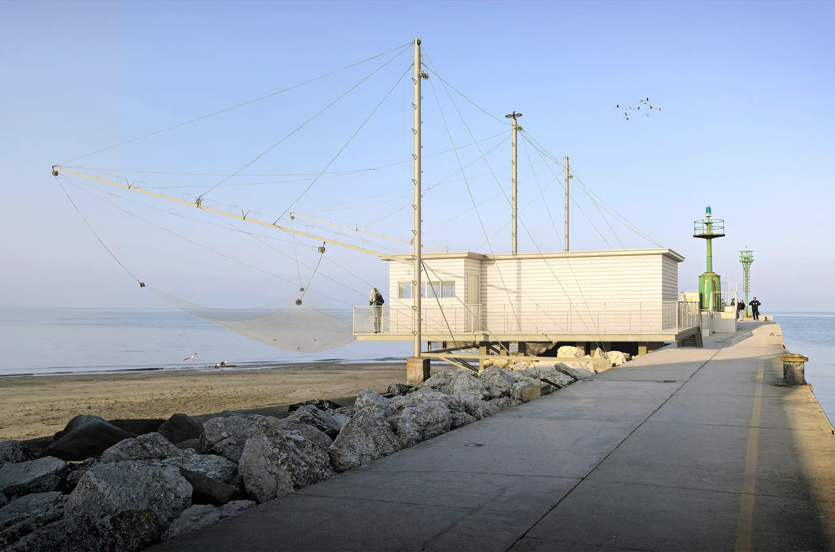 Pier leading out to the sea with a structured, modern fishing hut featuring taut cables and a large fishing net. The scene captures a serene winter sunset, an expansive view of the open water meeting the horizon, ideal for coastal architecture and peaceful seaside moments.