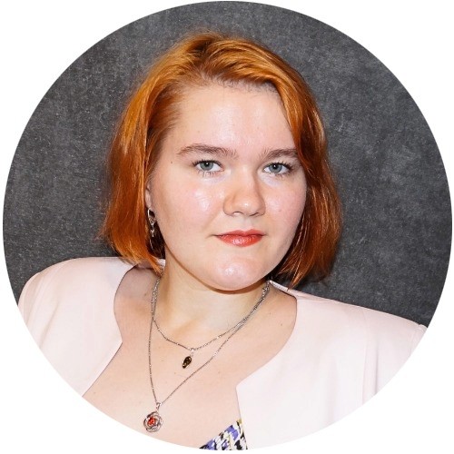 Close-up portrait of a freckled woman with soft pink hair and star earring, natural light, white tank top.