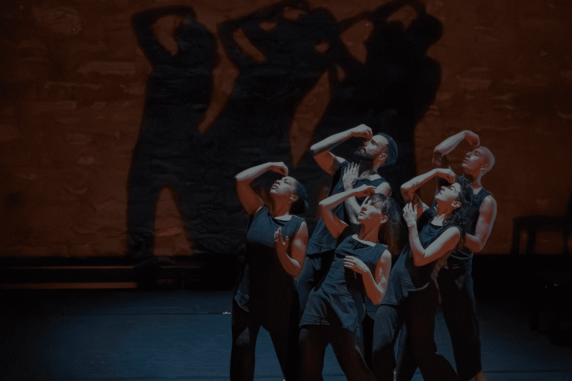 Company dancers performing ensemble choreography by Wynn Fricke against a dark wall with dramatic shadows. Photo by Bill Cameron.
