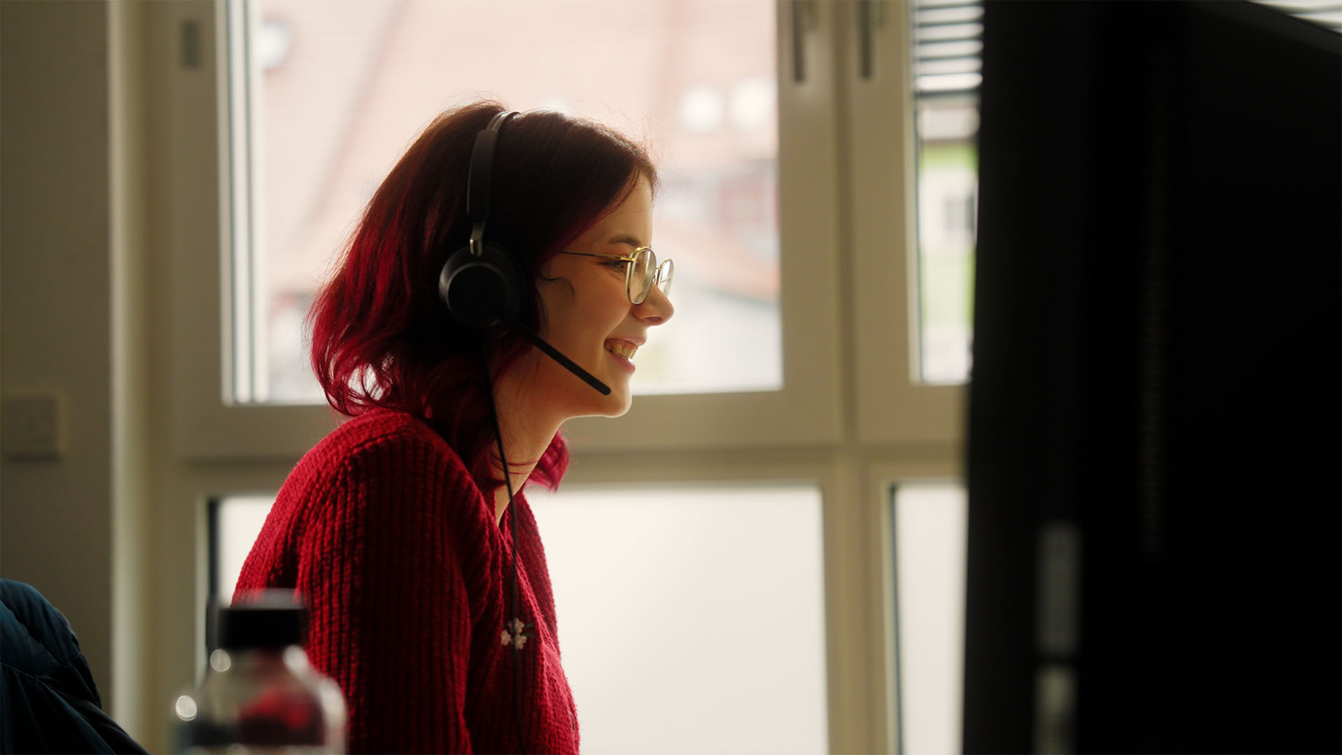 Woman with headset smiles at a computer, embodying filmproduction communication for strategic social media campaigns.