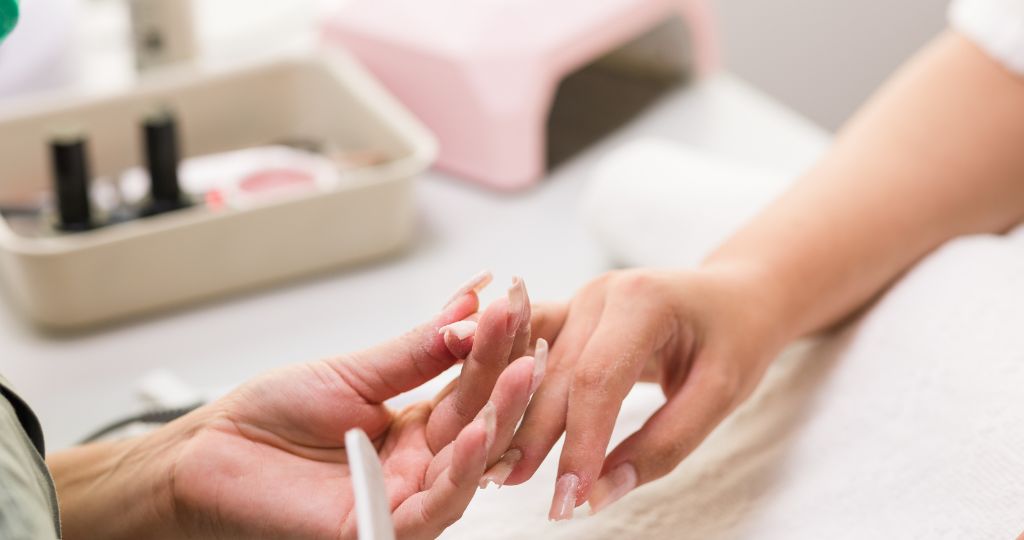 Nail technician filing customer's nails at a salon table.