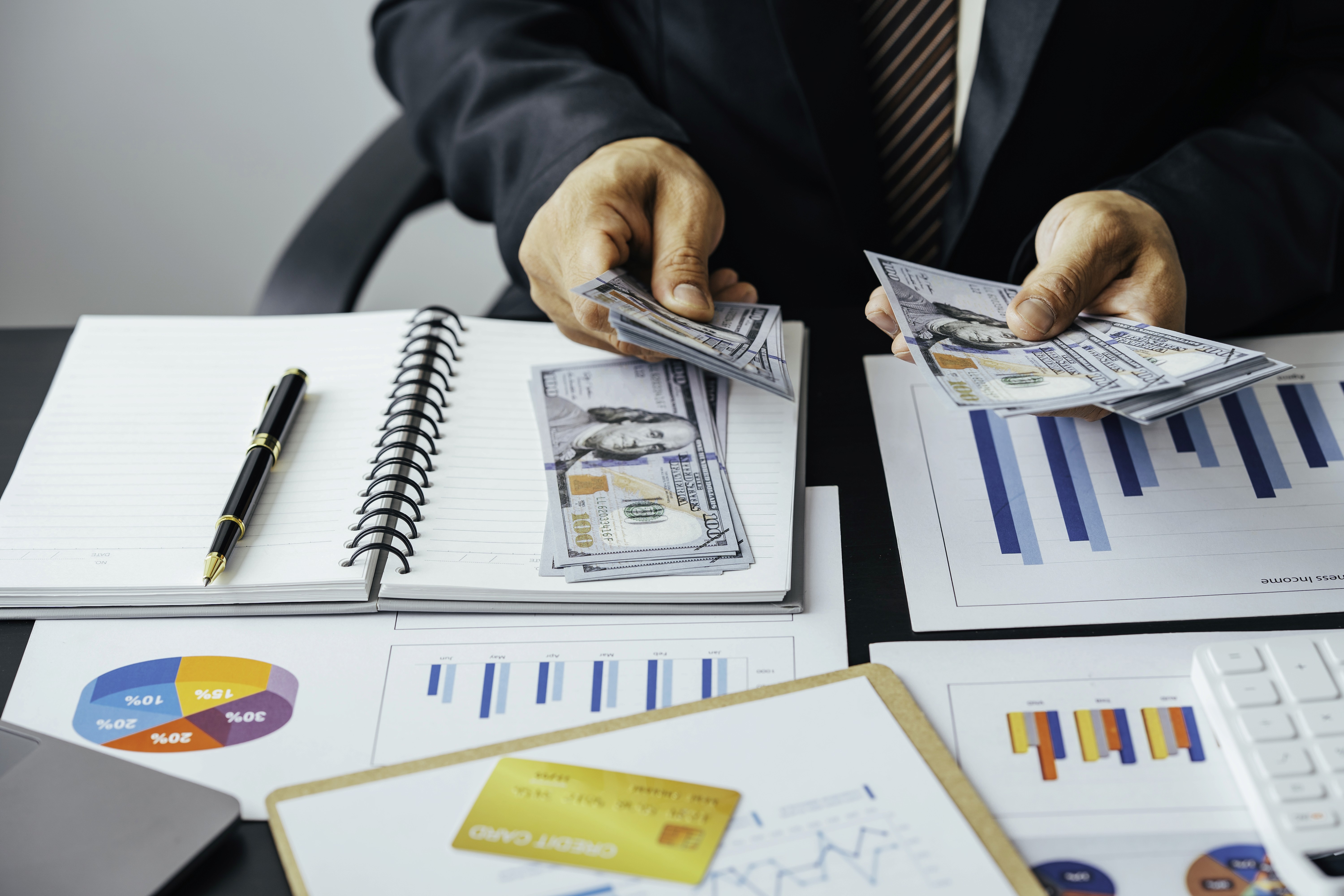 A person counting cash on a table full of charts