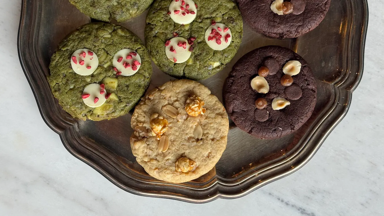 Assorted cookies on dark tray - matcha with white chocolate chips, chocolate with hazelnuts, and oatmeal walnut cookies