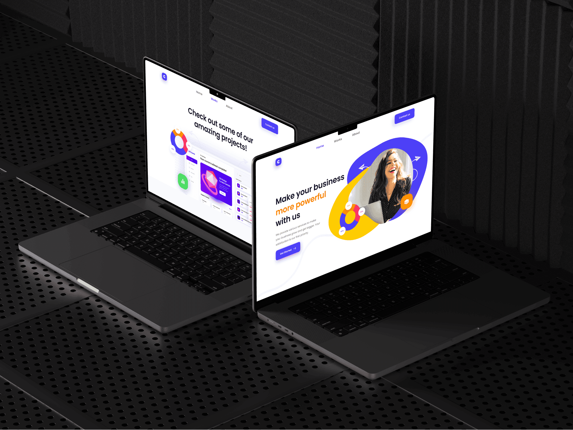 Two laptops display different pages of a professional portfolio website mockup on a dark, perforated metal surface