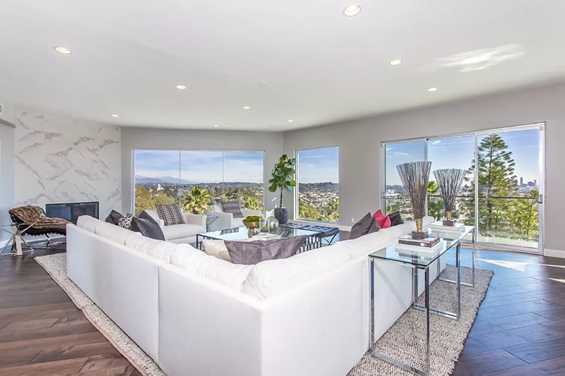 Aerial view of a small neighborhood with red-roofed houses nestled among lush green fields and winding roads. The scene feels peaceful and idyllic.
