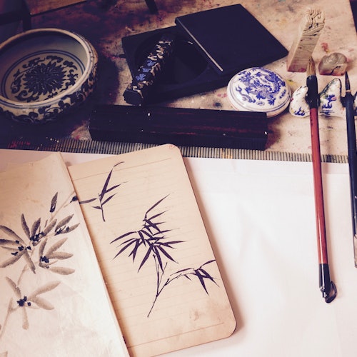 传统中国画的设置,包括毛笔、砚台、陶瓷以及一本展示竹子和叶子素描的笔记本。