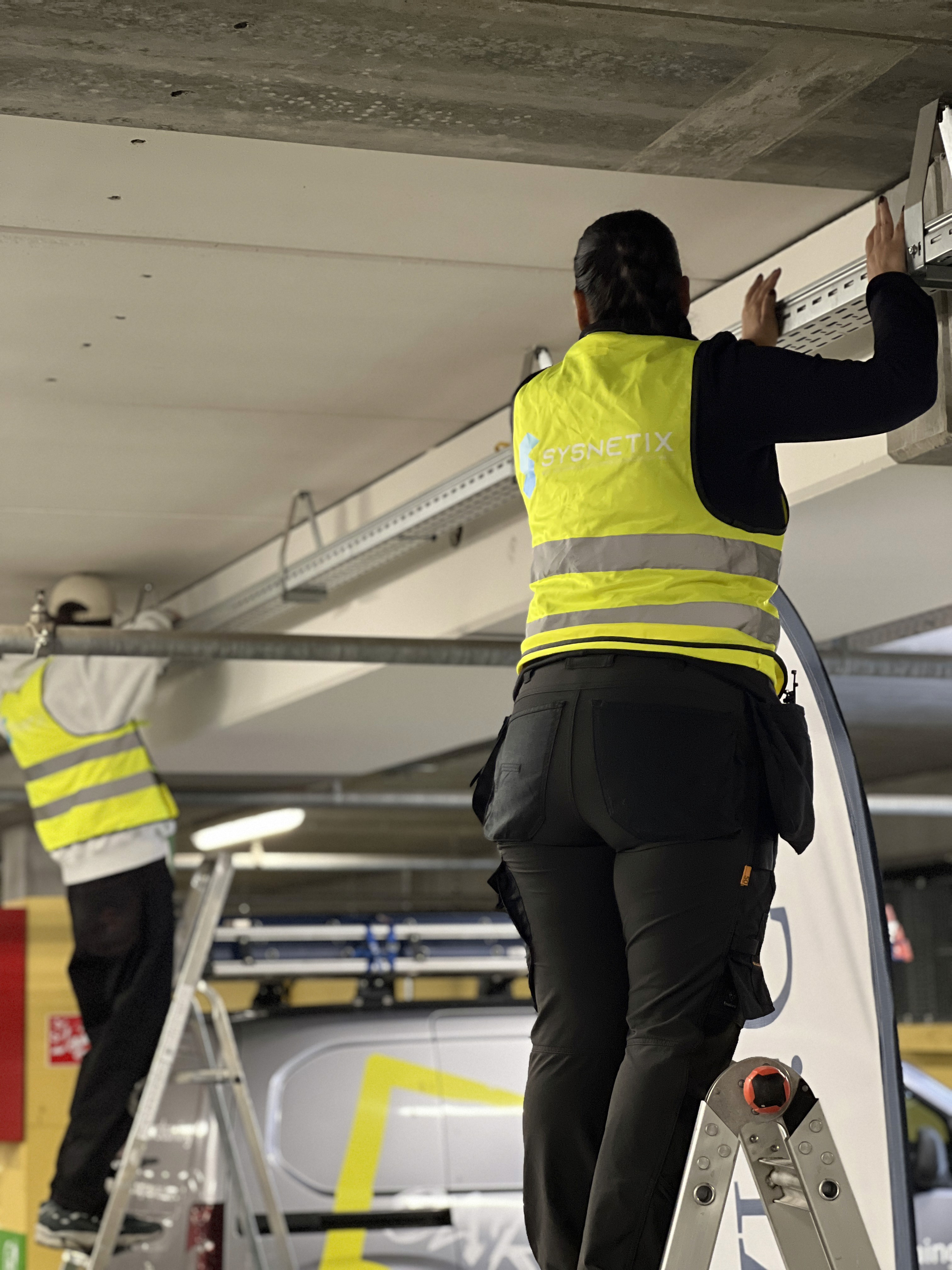 Technici leggen kabels langs het plafond van de parkeergarage