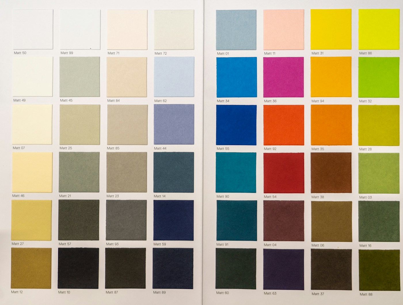A book of paint swatches open on a desk, from cream to deep green