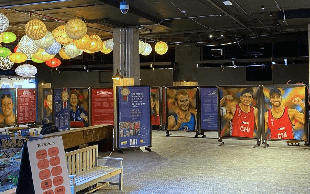 Activación de marca Score Energy Drink. Grupo de personas con latas de Score Energy Drink frente a la pintura de Eliseo Salazar en la exposición Leyendas del Deporte USACH.