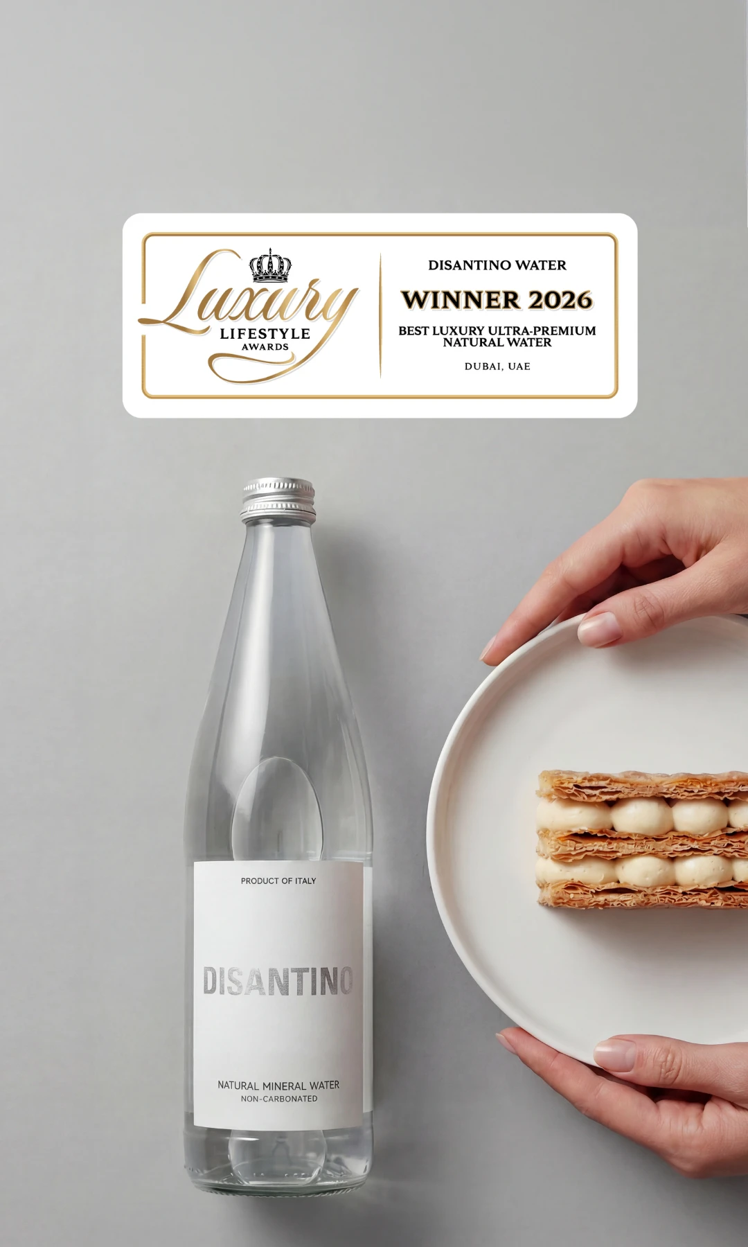 A marketing image of an overhead view of a DISANTINO water bottle next to a hand holding a plate with a layered pastry. A central gold badge reads "Luxury Lifestyle Awards Winner 2026: Best Luxury Ultra-Premium Natural Water, Dubai, UAE."