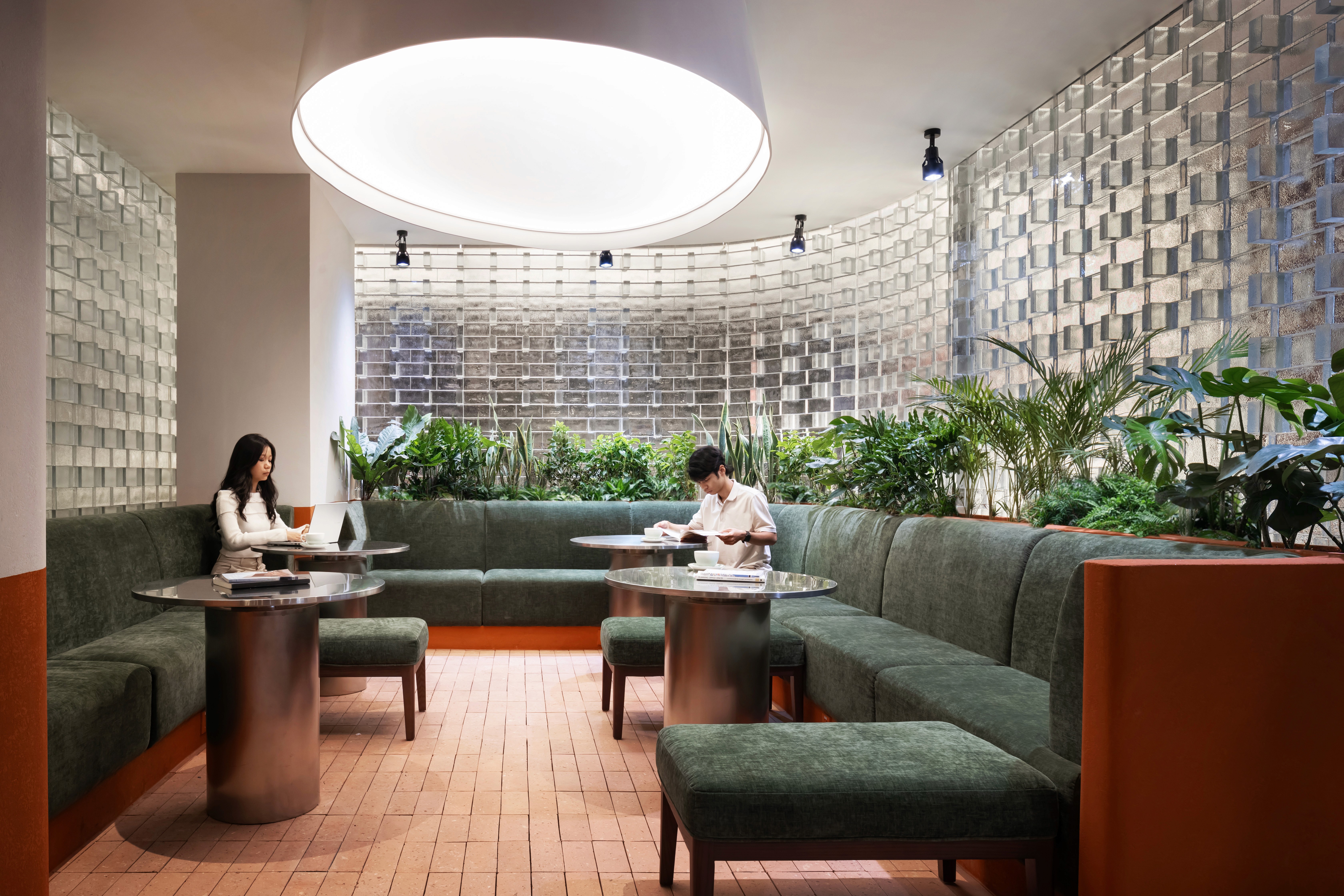 Indoor garden lounge with banquette seating, abundat planting, layout prioritising comfort, operational durability, translucent glass block, with large circular pendant lamp