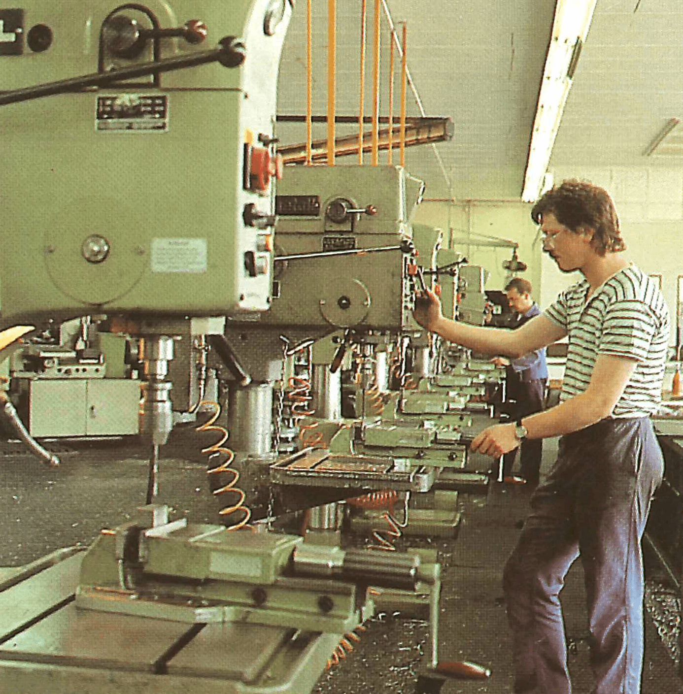 Industriehalle mit alten Bohrmaschinen. Ein Arbeiter bedient eine Bohrmaschine. Metallbearbeitung im Werk. 