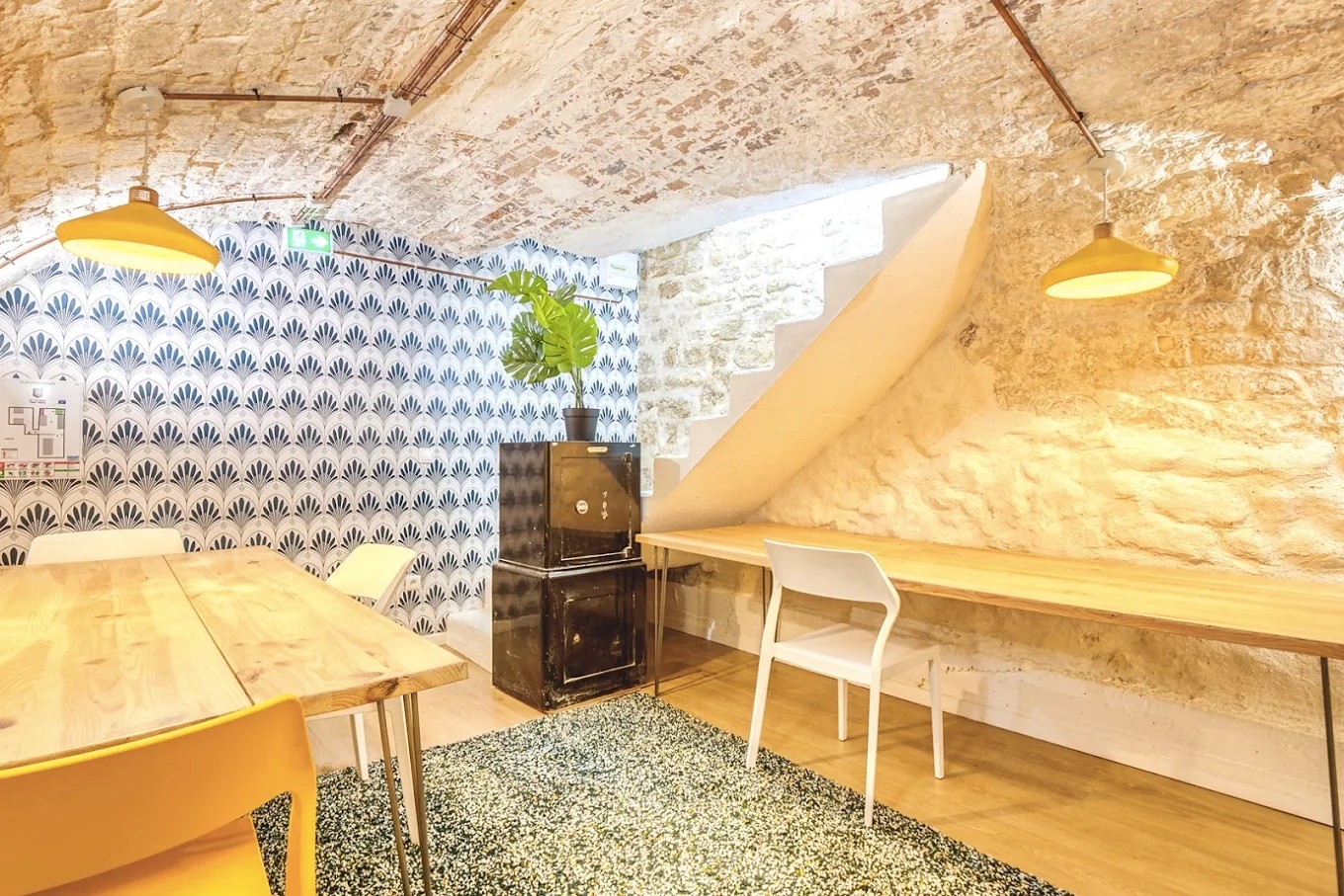 Aménagement de bureaux atypiques dans une cave voûtée en pierre avec plans de travail en bois et tapis vert.