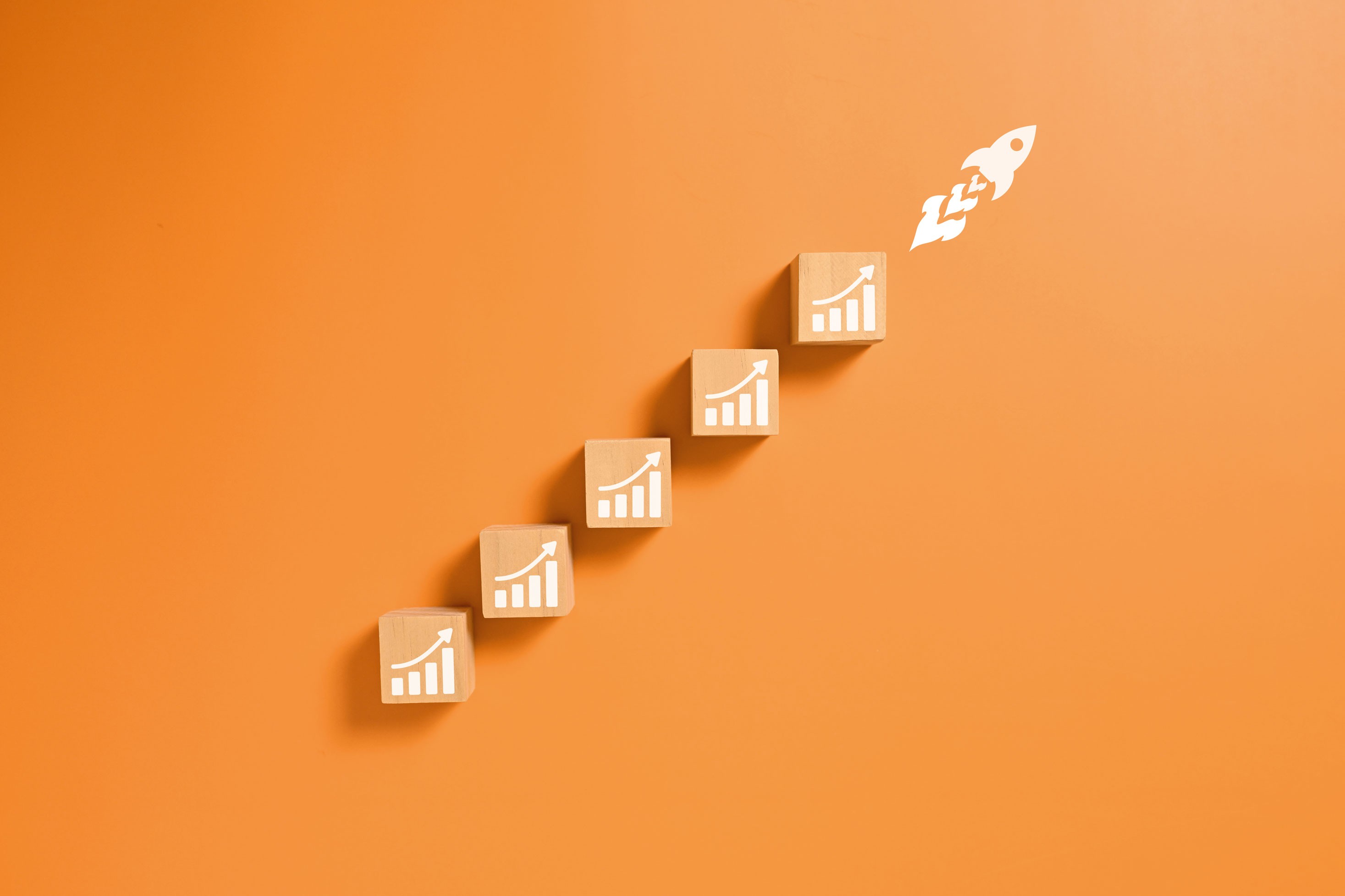 Drewniane klocki z ikonami wykresu ułożone w schody prowadzące do startującej rakiety