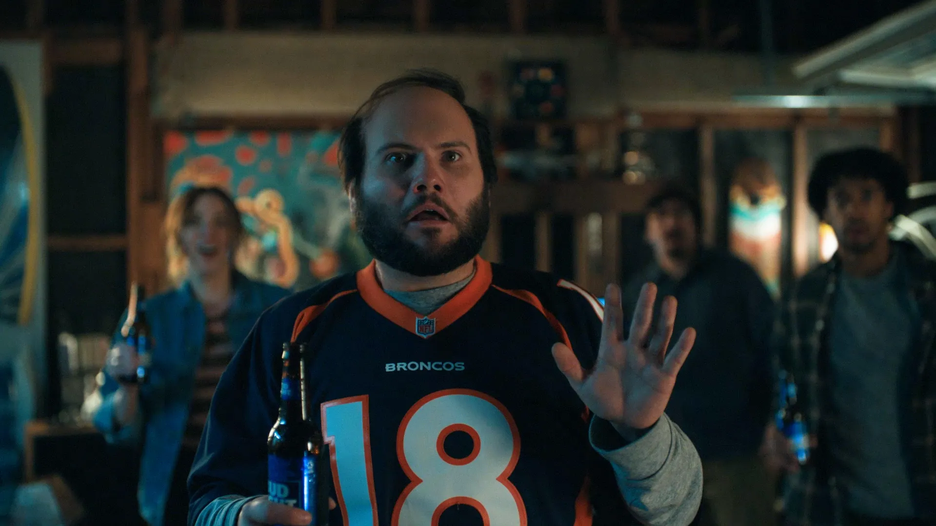 A person wearing a Broncos football jersey number 18, raising their hand in what appears to be a social gathering or bar setting with blurred background elements.