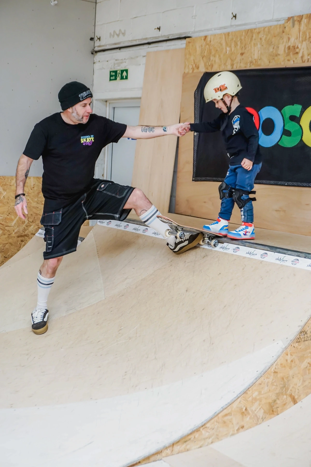 A skate coach helping a young child on inline skates at The Skate Farm indoor skatepark in Haywards Heath, Sussex