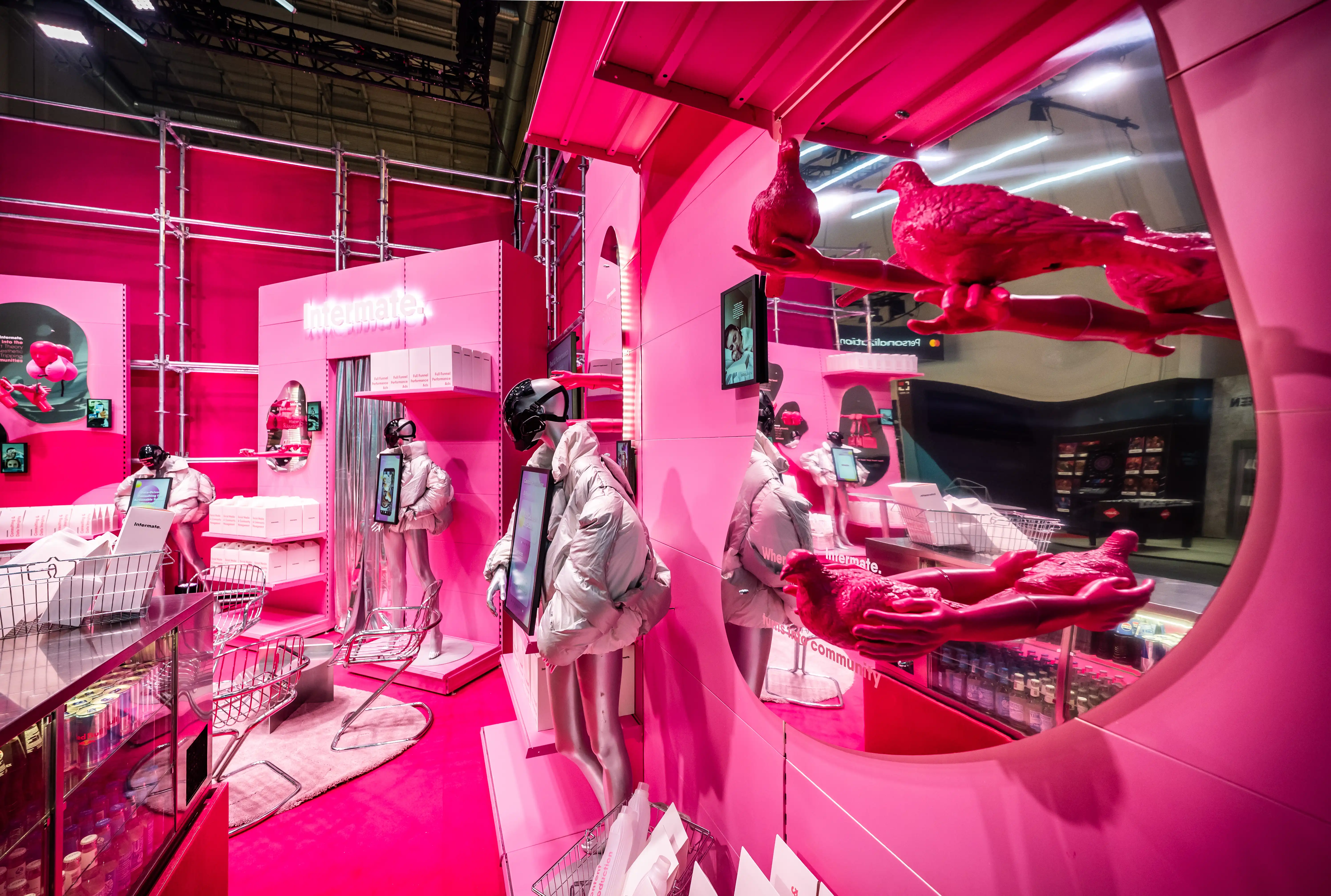 Magenta booth world of the Intermate Social Superstore with figures in white suits, pink birds and curved display windows.