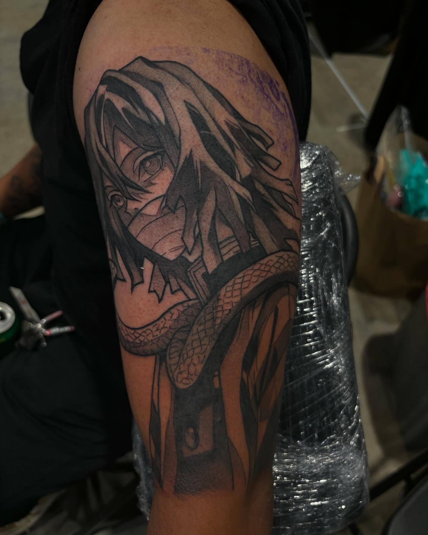 A grayscale anime-style tattoo of a character with spiky hair and a headband, holding a kunai.  The tattoo is on someone's forearm.