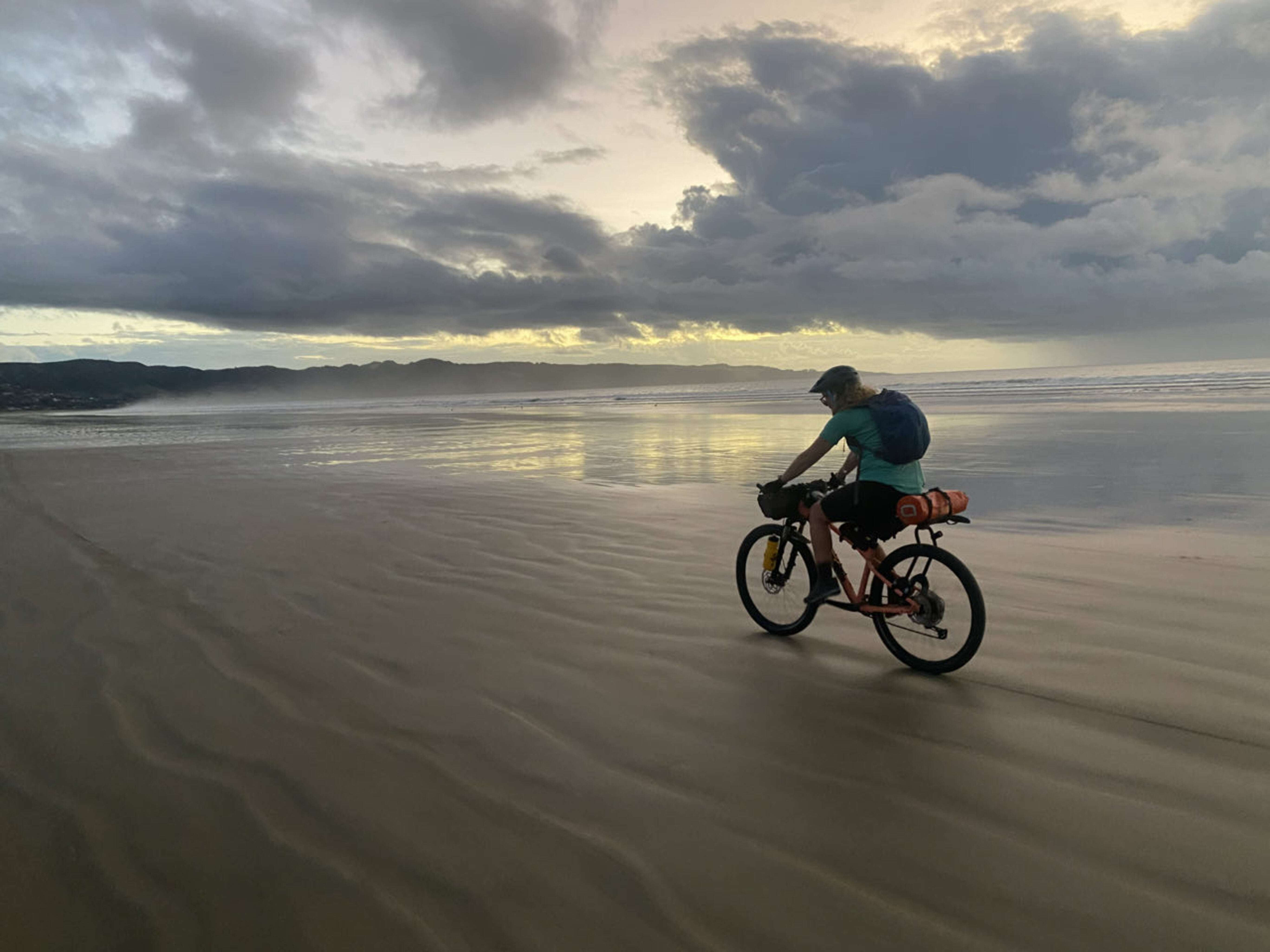 A woman cycles along a deserted beach in New Zealand