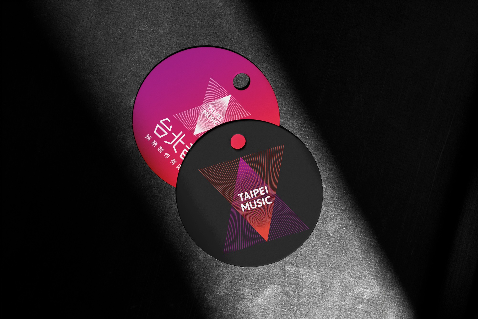 這張圖像展示了台北音樂的兩個圓形掛牌，一個是紅紫色背景，另一個是黑色背景，兩個掛牌上都有紫紅色漸層三角形的圖形和 "Taipei Music" 字樣的品牌識別。