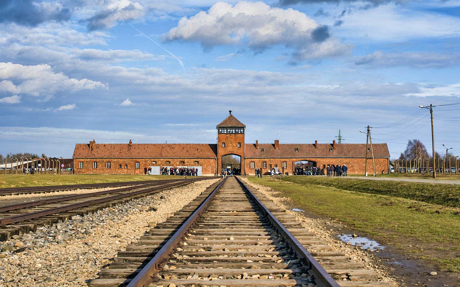 Tory kolejowe prowadzące do wejścia Muzeum Auschwitz-Birkenau pod błękitnym niebem.