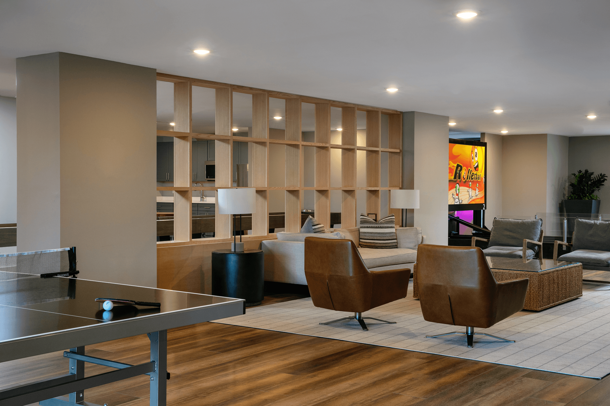 Modern living room with wood accents, stylish seating, and a bookshelf against a light-colored wall.