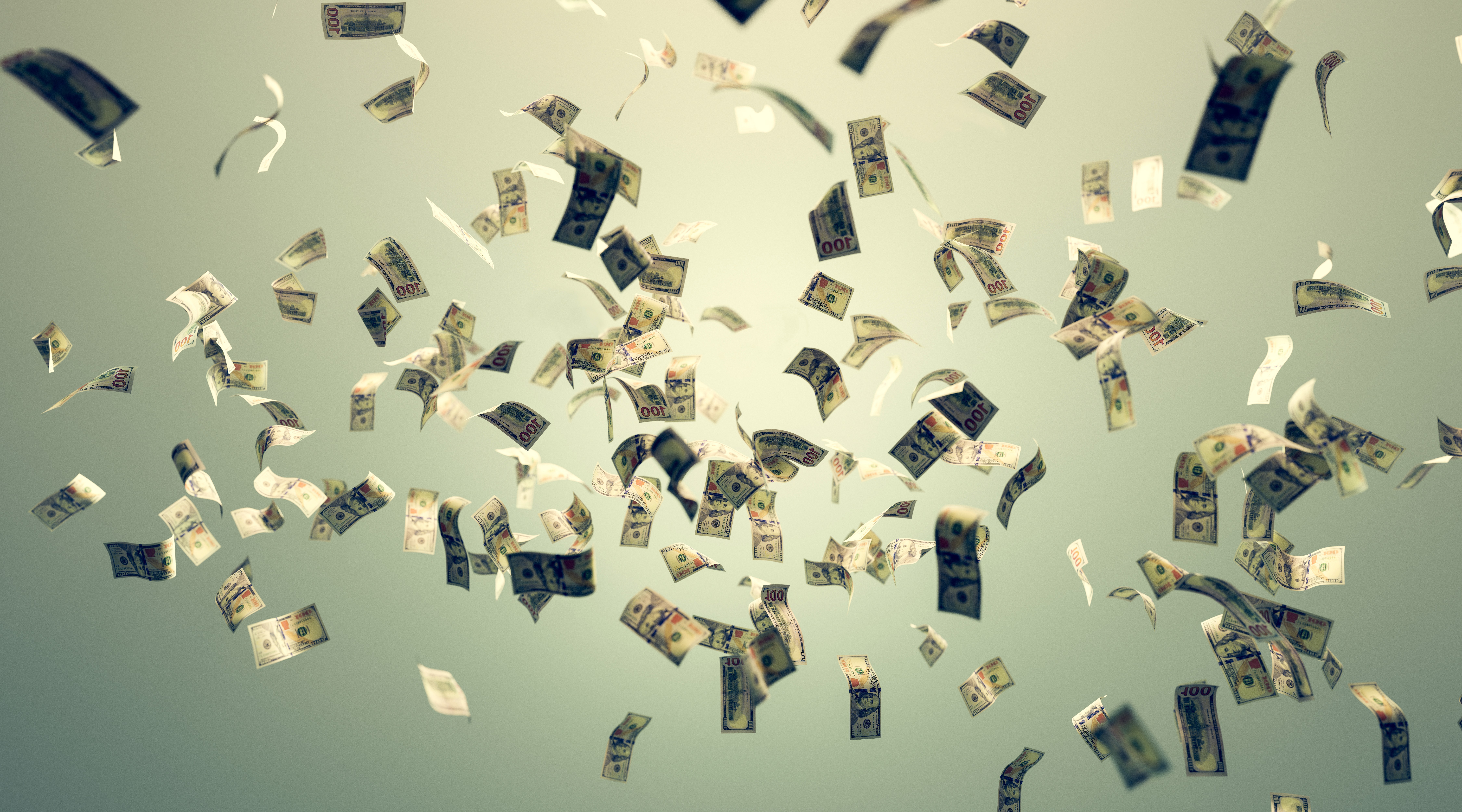 US dollar bills falling through the air against a muted green-grey background