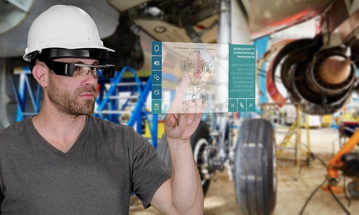  This image features a worker in a safety helmet and augmented reality (AR) glasses interacting with a holographic interface in an industrial setting, likely an aircraft maintenance environment. The transparent overlay displays technical schematics, tools, and instructions, blending seamlessly with the physical workspace around him. This depiction highlights the innovative role of VR manufacturing and AR in transforming complex industrial operations.  The use of VR manufacturing in scenarios like this empowers technicians to access real-time data, visualizations, and step-by-step guides without the need for physical manuals or external devices. By integrating virtual tools with real-world tasks, professionals can improve precision, reduce errors, and enhance productivity. This application is especially beneficial in sectors such as aerospace, where accuracy and efficiency are critical.  VR manufacturing also allows industries to streamline training processes by immersing new employees in realistic, interactive simulations of equipment or procedures. This approach not only reduces downtime but also minimizes risk by preparing workers for real-world scenarios in a safe, controlled environment. The fusion of AR and VR manufacturing is revolutionizing how industries approach maintenance, production, and training, setting new benchmarks for innovation and operational excellence.