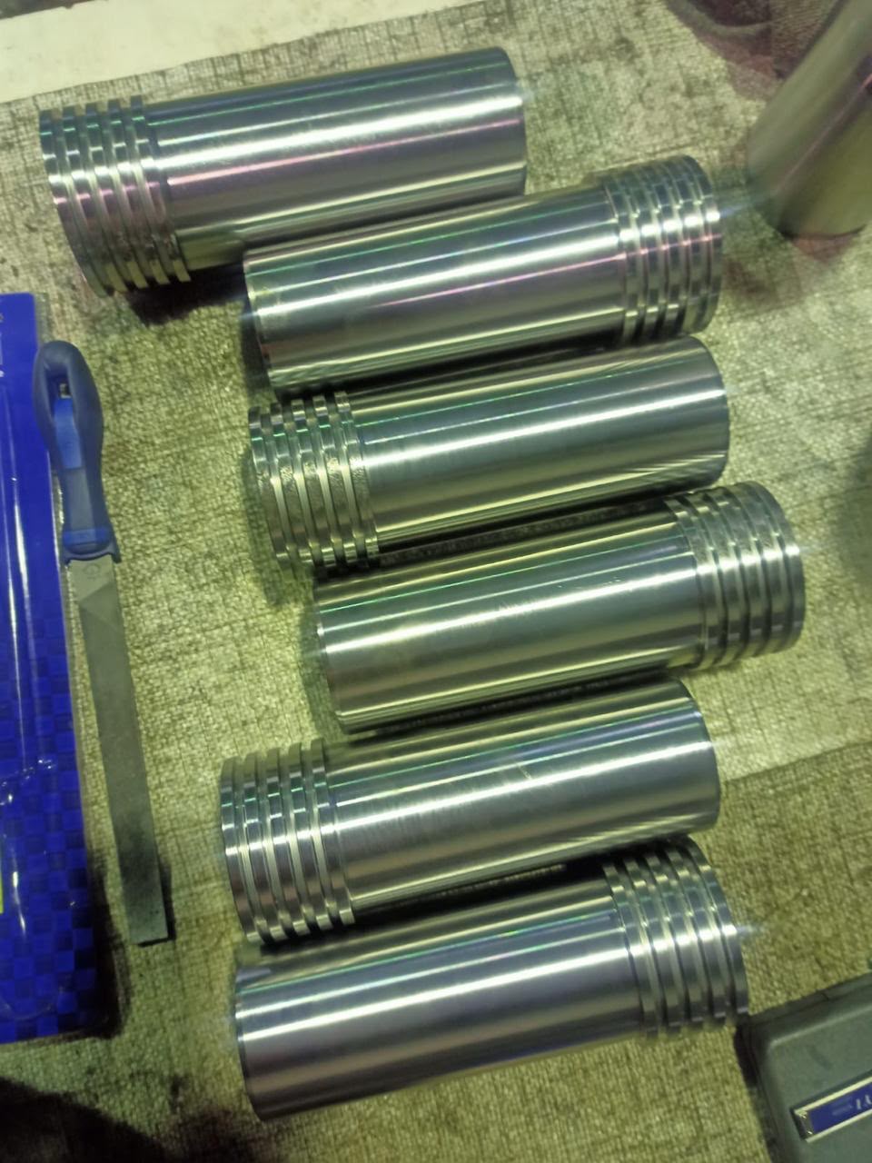 Batch of finished precision-machined steel shafts with grooved ends on a workbench.
